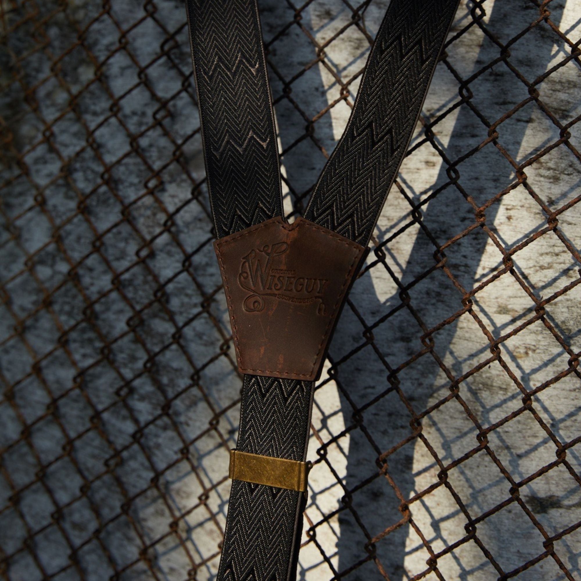 Close-up of Wiseguy Original herringbone pattern elastic suspenders with fence as background.