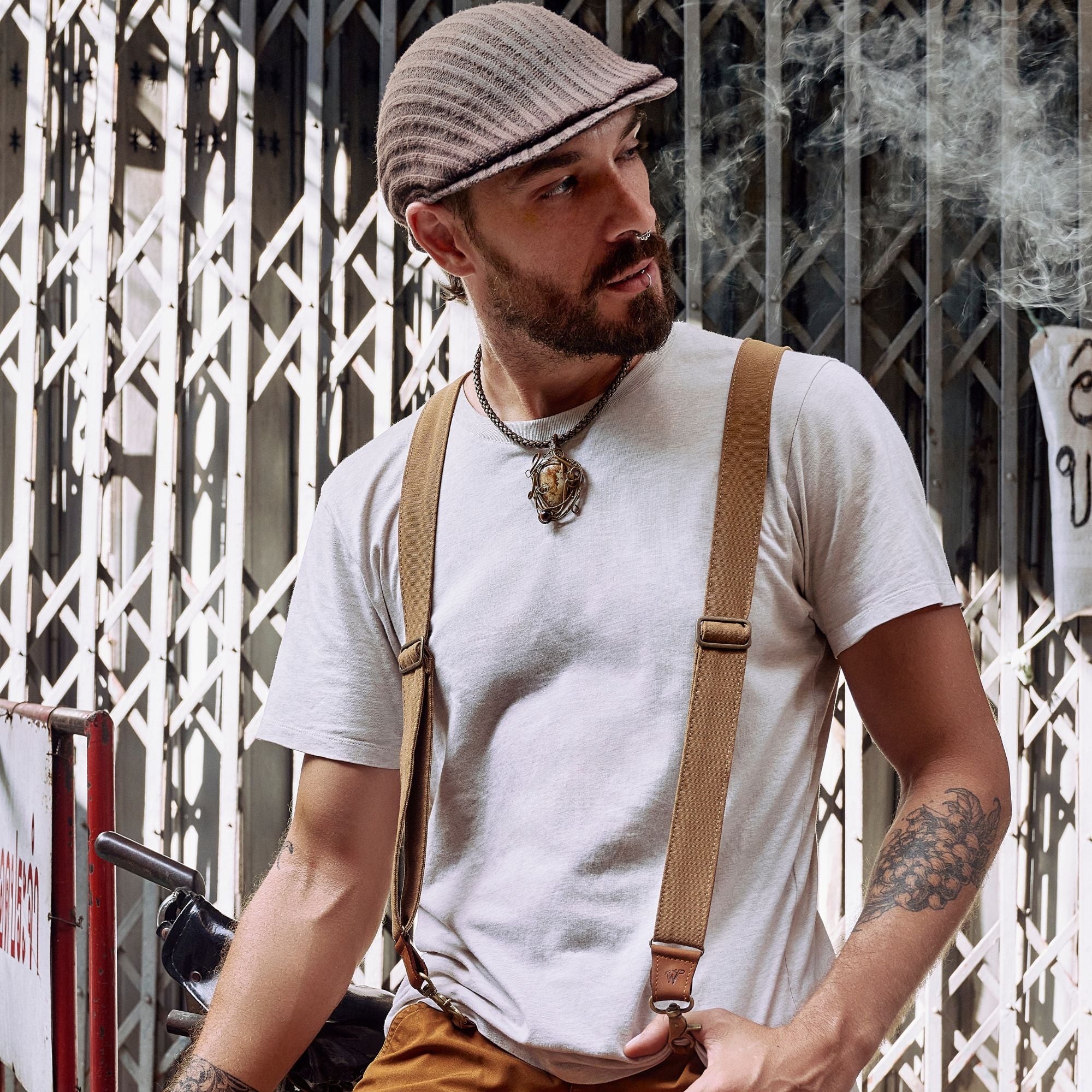 Man in front of gate wearing a flat cap and Wiseguy Original Suspenders.