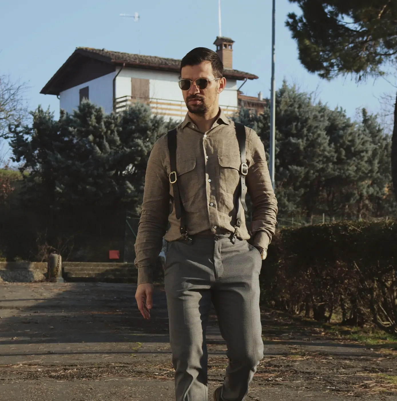 Man wearing black Wiseguy Hershel suspenders over a beige linen shirt and grey trousers, walking outdoors